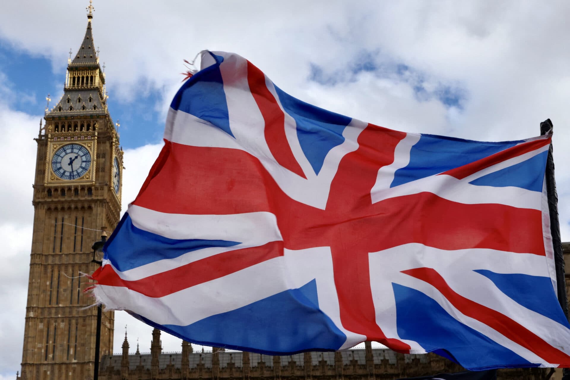 Et Union Jack-flagg vaier i forgrunnen med Elizabeth Tower og klokken, ofte kjent som Big Ben, i bakgrunnen mot en delvis overskyet himmel.